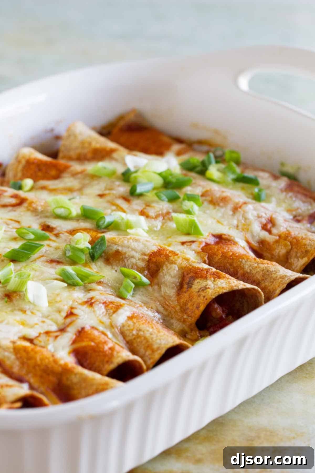 Hearty Sausage and Bean Enchiladas 2 A baking dish filled with golden-brown sausage and bean enchiladas, generously topped with red enchilada sauce, melted Monterey Jack cheese, and fresh green onions, ready to serve.