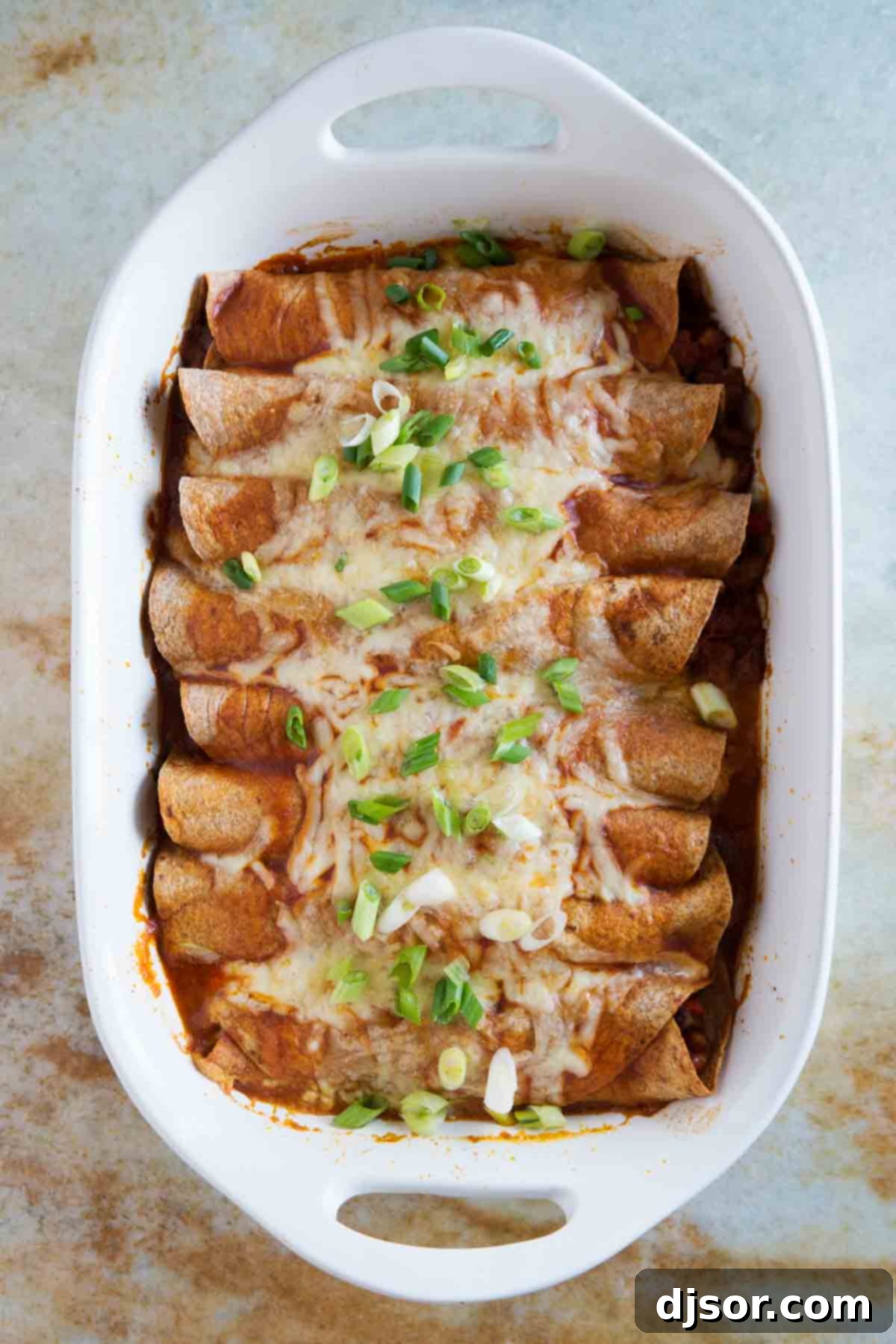 Hearty Sausage and Bean Enchiladas 3 A white casserole dish filled with neatly rolled Sausage and Bean Enchiladas, showing the rich filling peeking from some ends, before being covered with sauce and cheese.