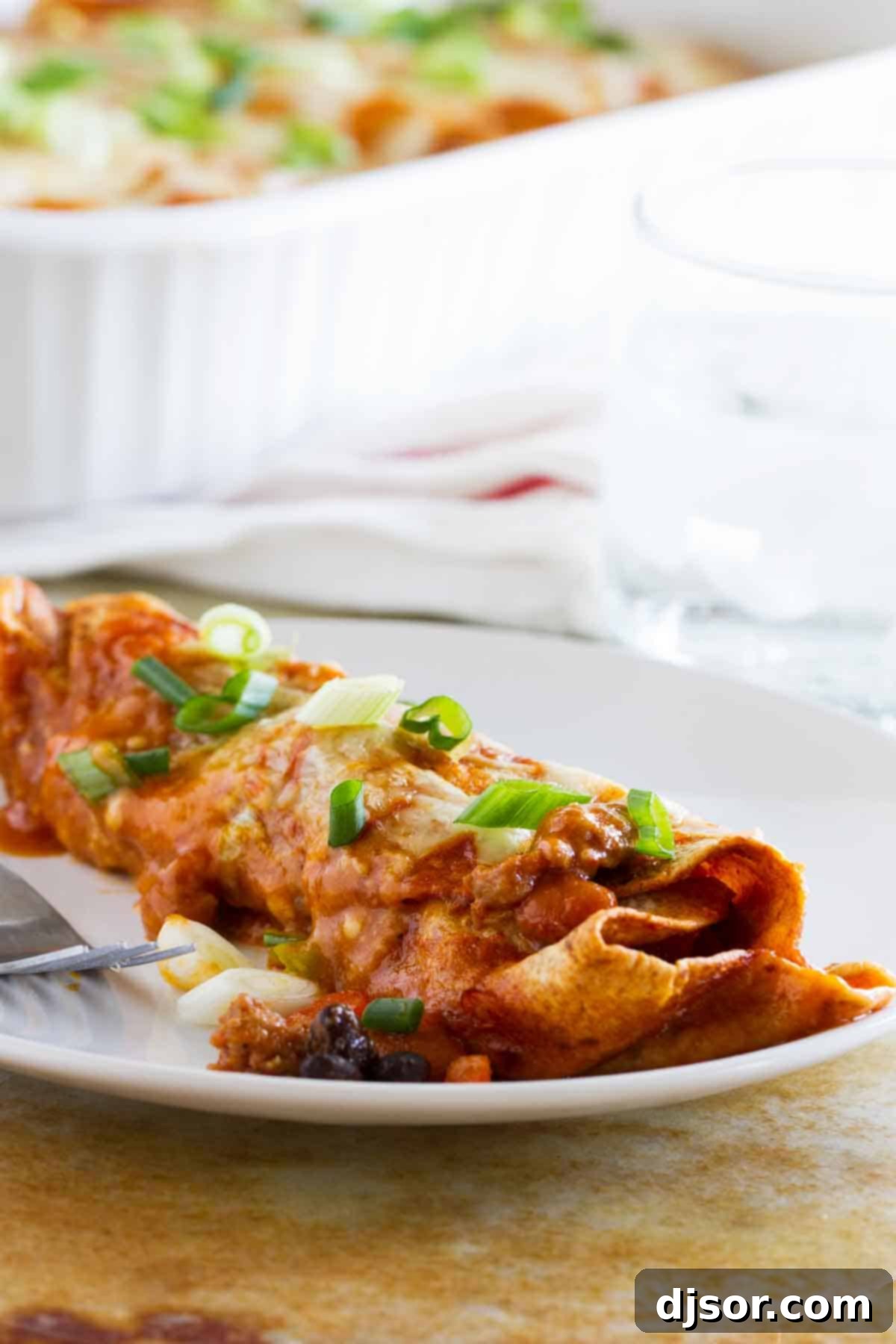 Hearty Sausage and Bean Enchiladas 4 A single Sausage and Bean Enchilada on a white plate, showcasing the rich filling, melted cheese, and a garnish of fresh green onions and cilantro.