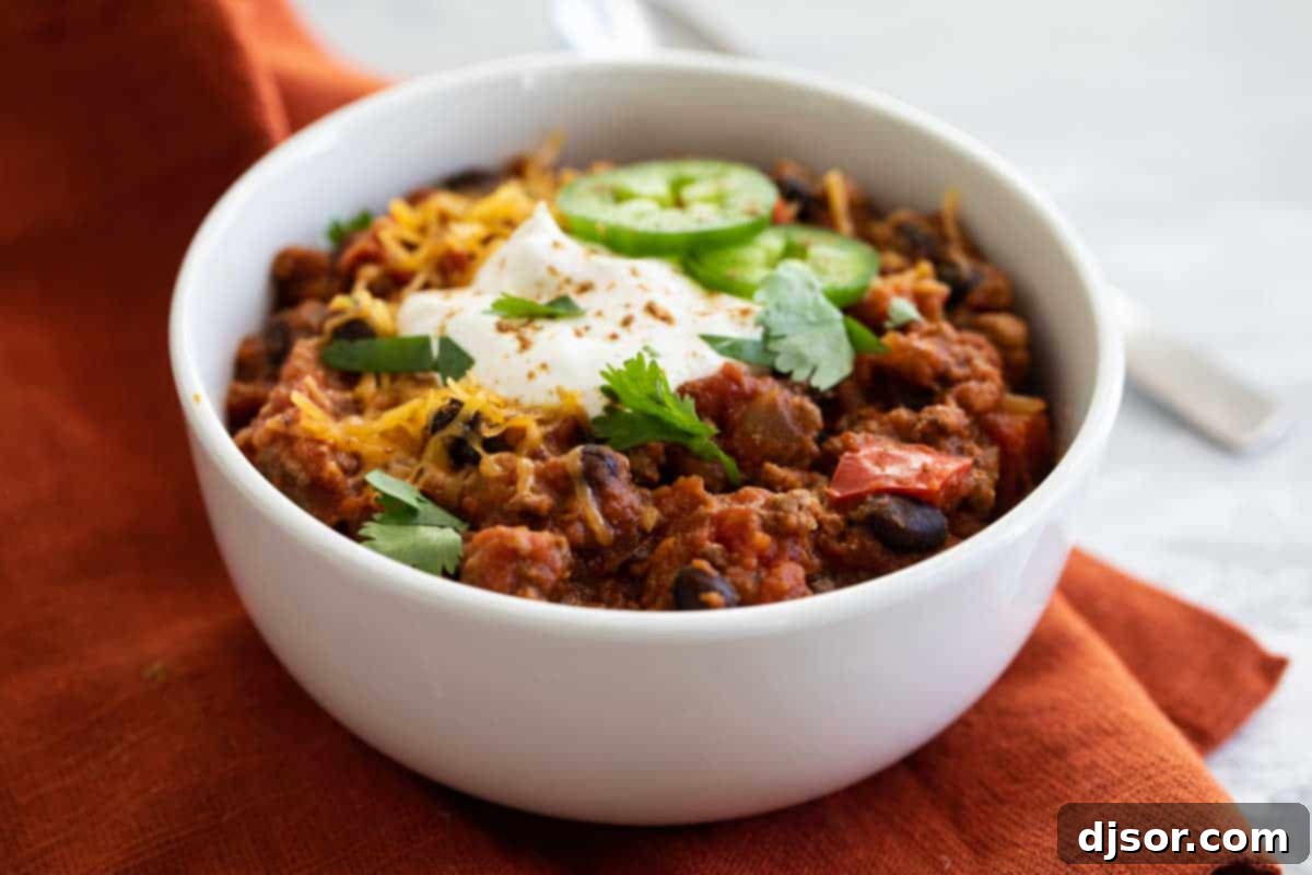 A steaming bowl of slow cooker pumpkin chili, garnished with fresh cilantro and a dollop of sour cream, resting on a rustic wooden table.