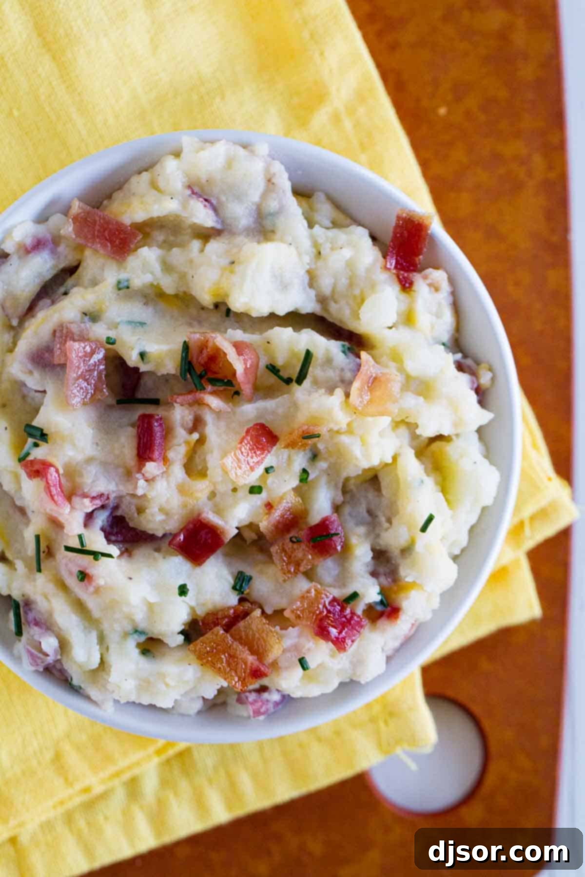 Bowl of creamy loaded mashed potatoes with visible skins, bacon, and chives