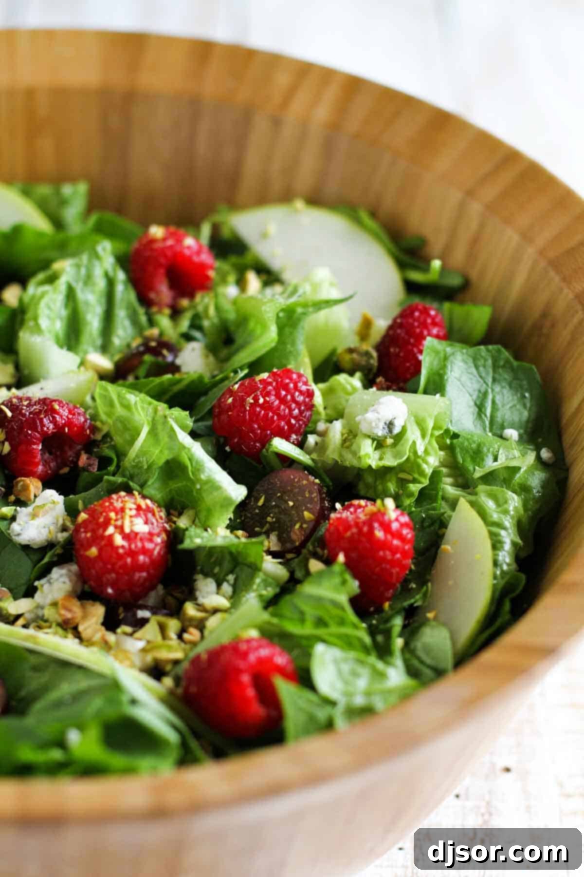 This Raspberry Spinach Salad has spinach, romaine, grapes, dried cranberries, pear, raspberries, blue cheese and pistachios and is served with a homemade raspberry vinaigrette. Red Raspberry Spinach Salad with Raspberry Vinaigrette in a wooden bowl.