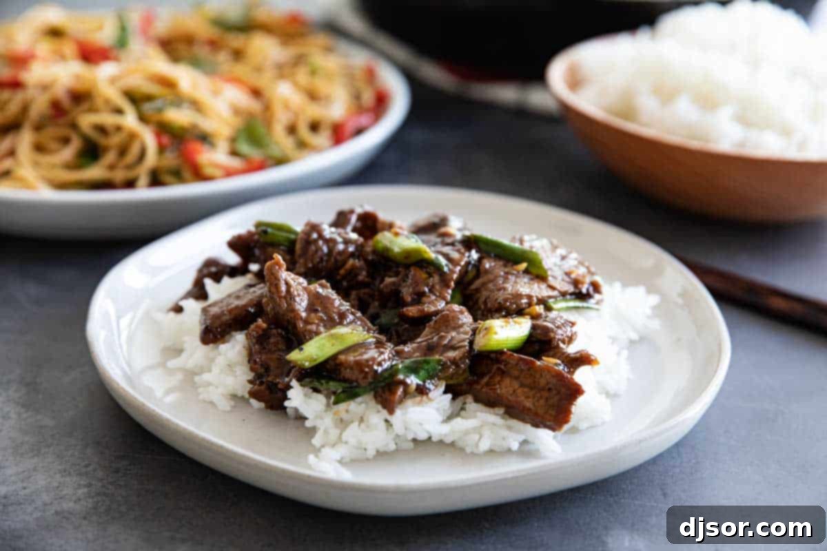 Mongolian Beef over rice on a white plate, garnished with green onions and sesame seeds.