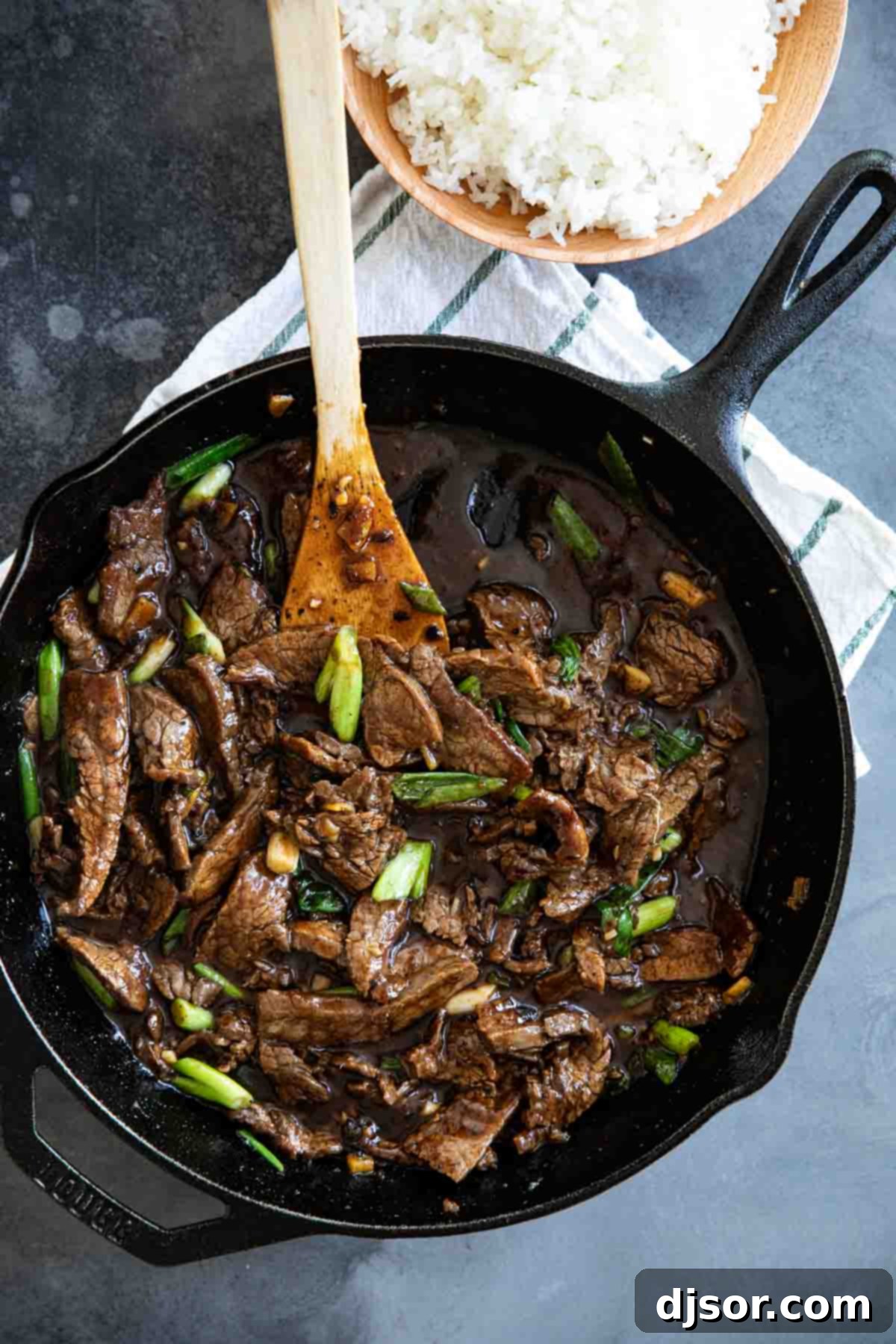 Mongolian Beef in a cast iron skillet, garnished with green onions and sesame seeds.