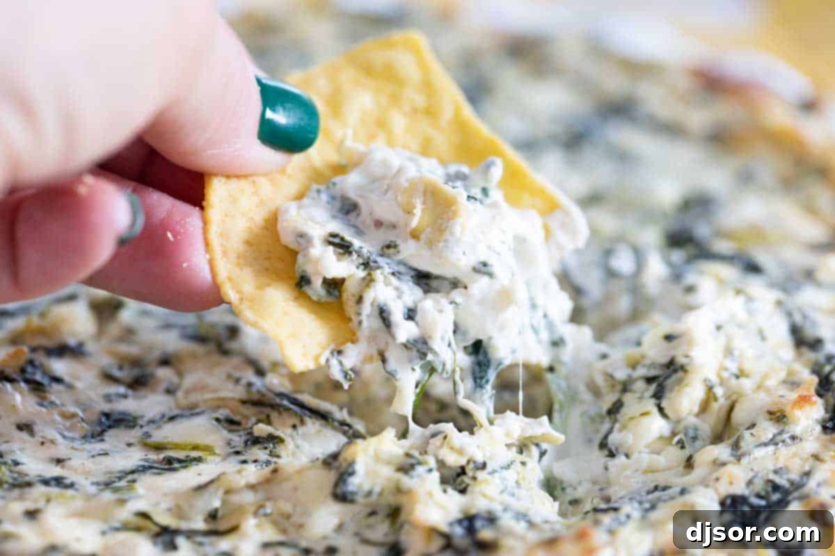A serving of creamy and cheesy spinach artichoke dip on a tortilla chip, ready to be enjoyed as a party appetizer.