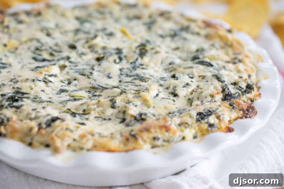 A baking dish filled with hot, bubbly, golden-brown spinach artichoke dip, freshly out of the oven.