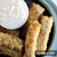 Cheeseburger Crunch Rolls 11 A plate featuring a stack of golden-brown Cheeseburger Eggrolls, accompanied by a small dish of Russian dipping sauce and fresh herbs for garnish.