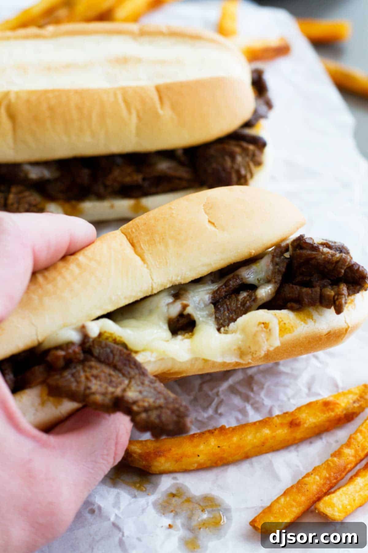 A hand holding a perfectly assembled Spicy Cajun Cheesesteak Sandwich, ready to be enjoyed.