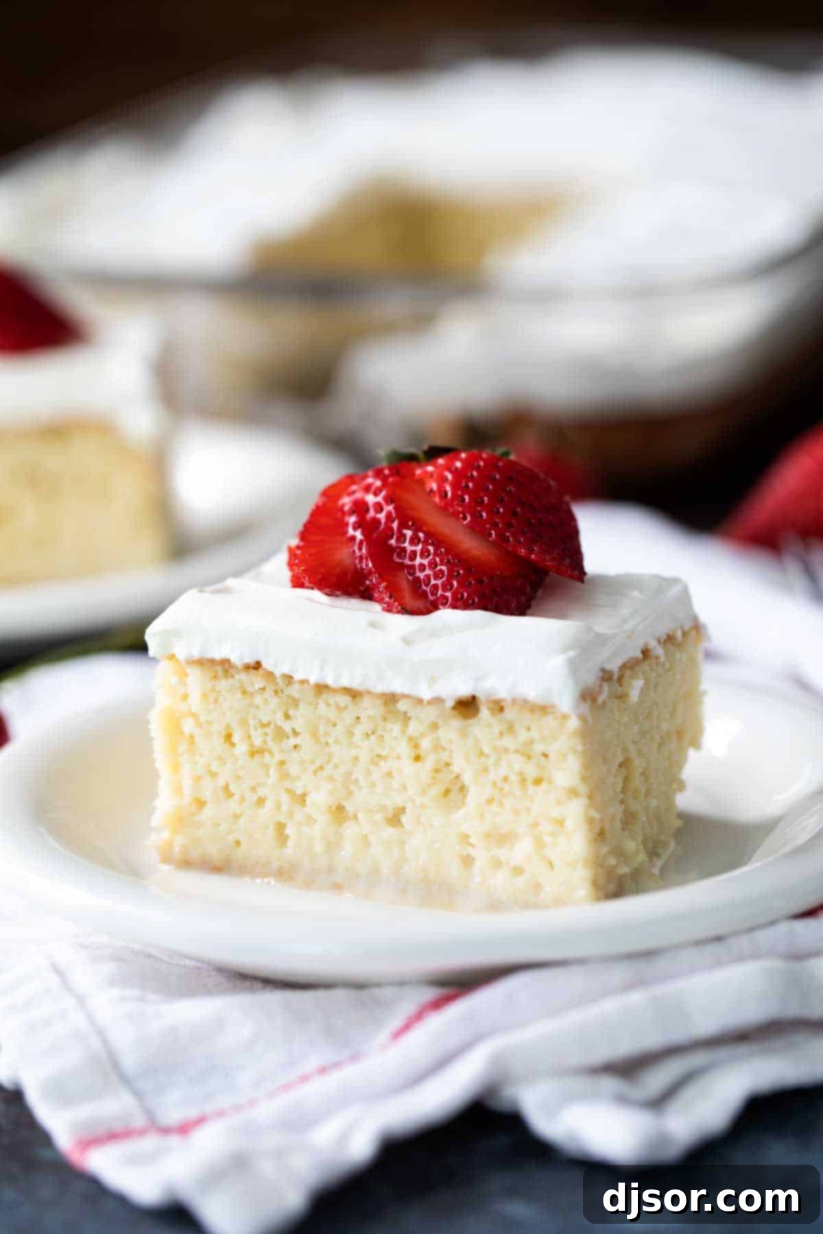 A beautifully presented slice of homemade Tres Leches Cake, garnished with a fresh strawberry, highlighting its moist texture and creamy topping.