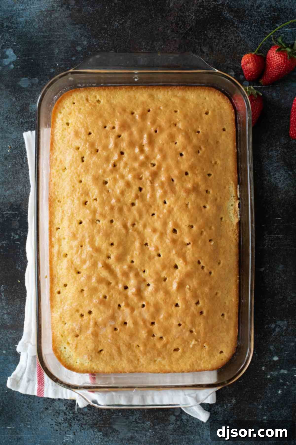 Close-up shot of a baked cake being pierced with a fork, preparing it to absorb the three-milk mixture for Tres Leches Cake.