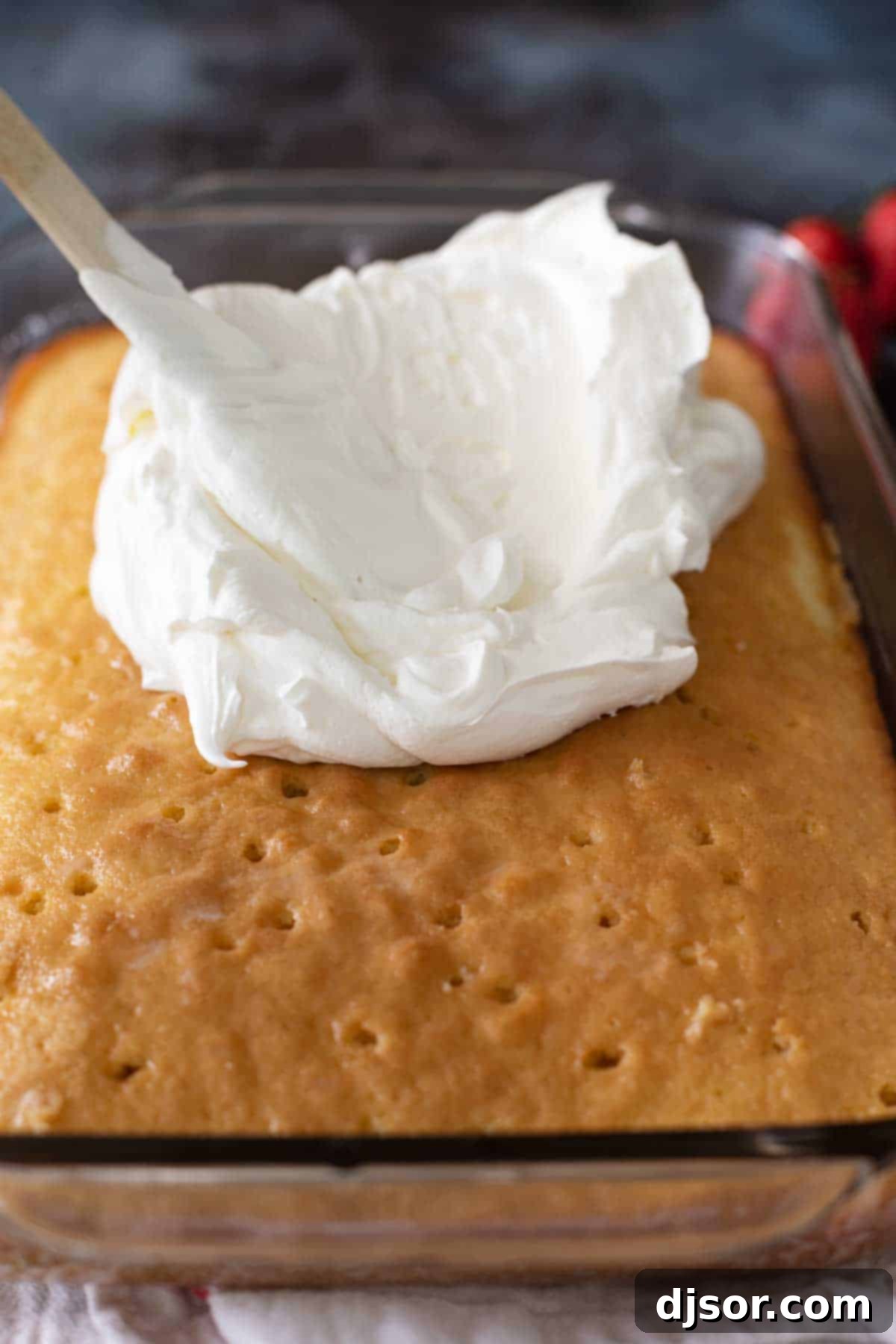 A Tres Leches Cake generously topped with freshly whipped cream, showing its delicious texture and inviting presentation.