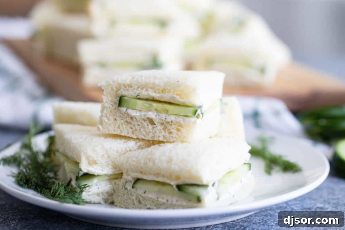 Stacked cucumber sandwiches on a white plate, garnished with fresh dill, ready to be served as an appetizer for lunch, brunch, or a party.