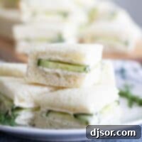 Stacked cucumber sandwiches on a white plate, garnished with fresh dill.