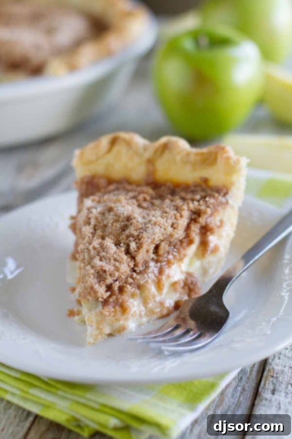 Crafting Your Perfect Thanksgiving 10 A perfect slice of Sour Cream Apple Pie on a white plate, revealing layers of spiced apples and crumbly streusel topping, with a fork ready to dig in.
