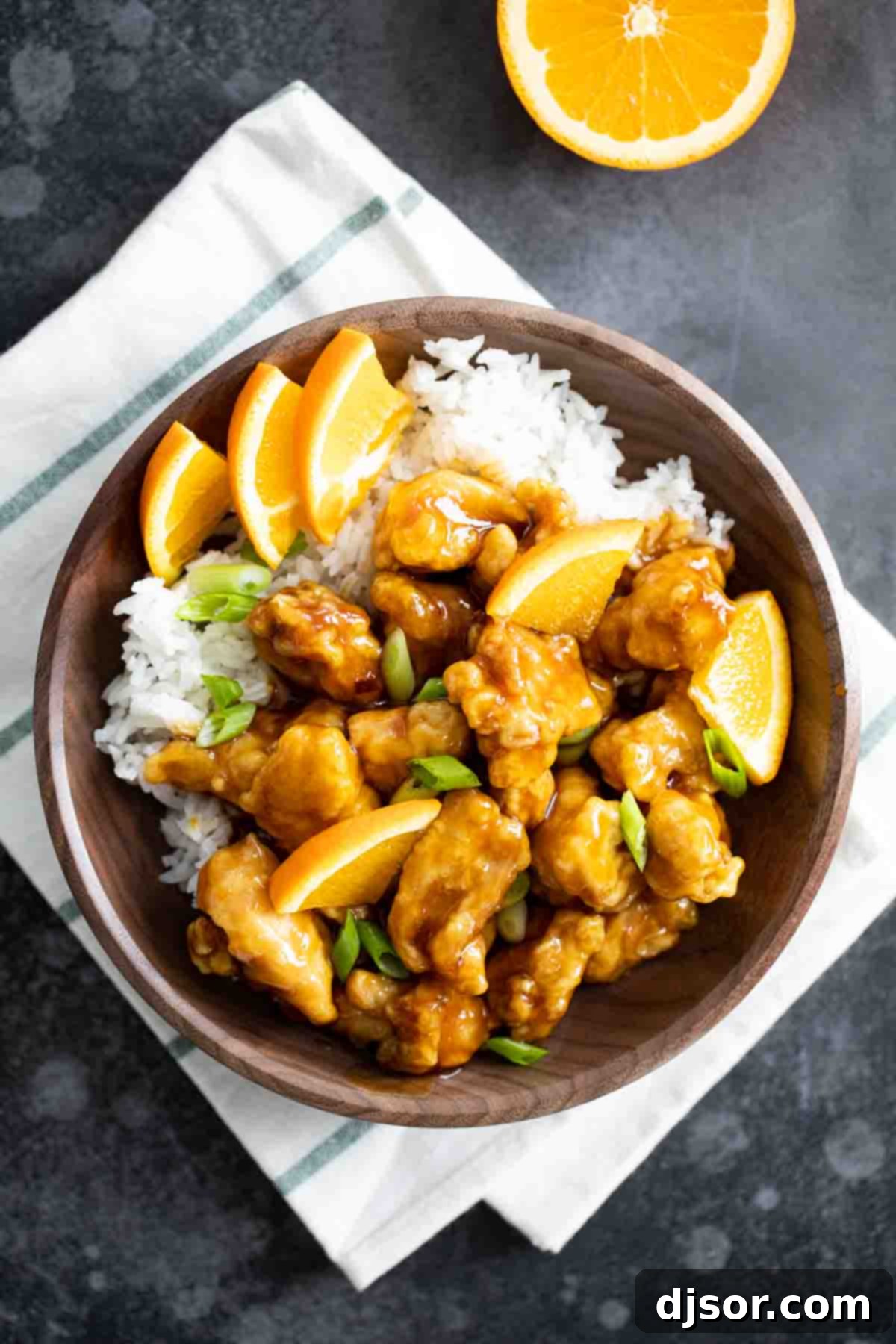 Enjoying the Best Homemade Orange Chicken – A Family Favorite! An inviting overhead view of a serving bowl filled with homemade orange chicken, steamed white rice, and a sprinkle of green onions.