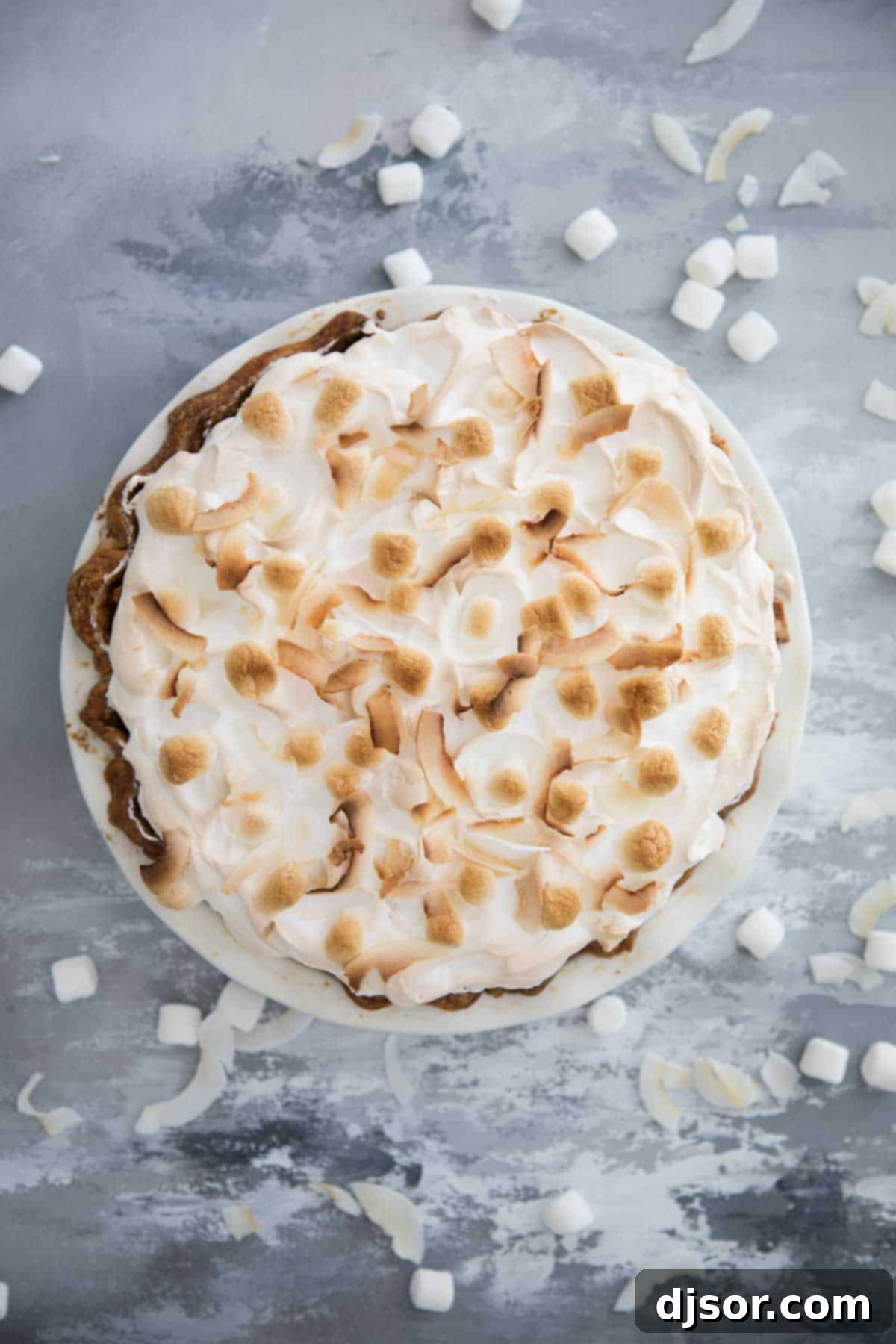 Take your pie game up a step with this Sweet Potato Pie with Marshmallow Coconut Meringue. A rich, smooth sweet potato pie is topped with a tall marshmallow meringue. A bit of coconut tops off this show stopping pie recipe. An overhead view of a perfectly baked Sweet Potato Pie, generously topped with a golden, toasted marshmallow coconut meringue, showcasing its impressive height and texture.