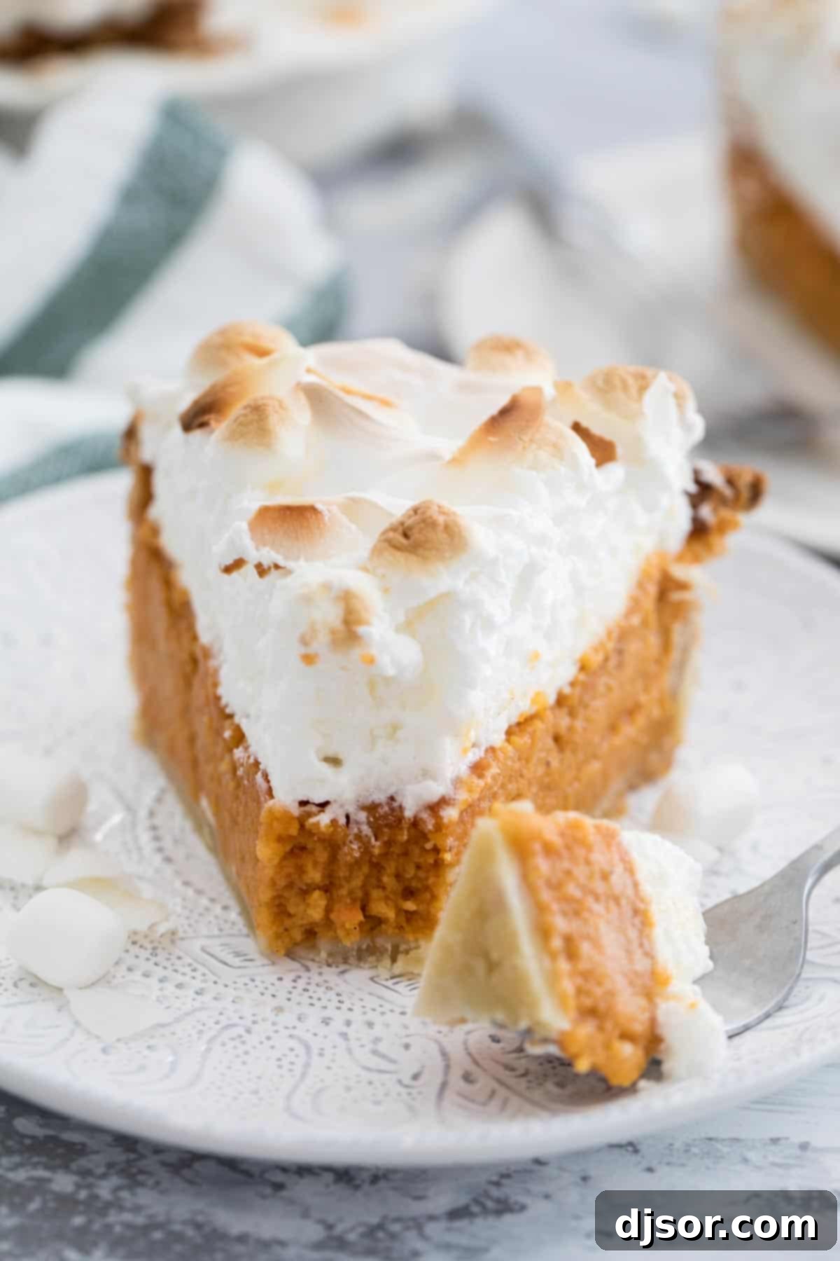 Take your pie game up a step with this Sweet Potato Pie with Marshmallow Coconut Meringue. A rich, smooth sweet potato pie is topped with a tall marshmallow meringue. A bit of coconut tops off this show stopping pie recipe. A fork takes a delicious bite out of a slice of Sweet Potato Pie with Marshmallow Coconut Meringue, highlighting its creamy filling and airy topping.