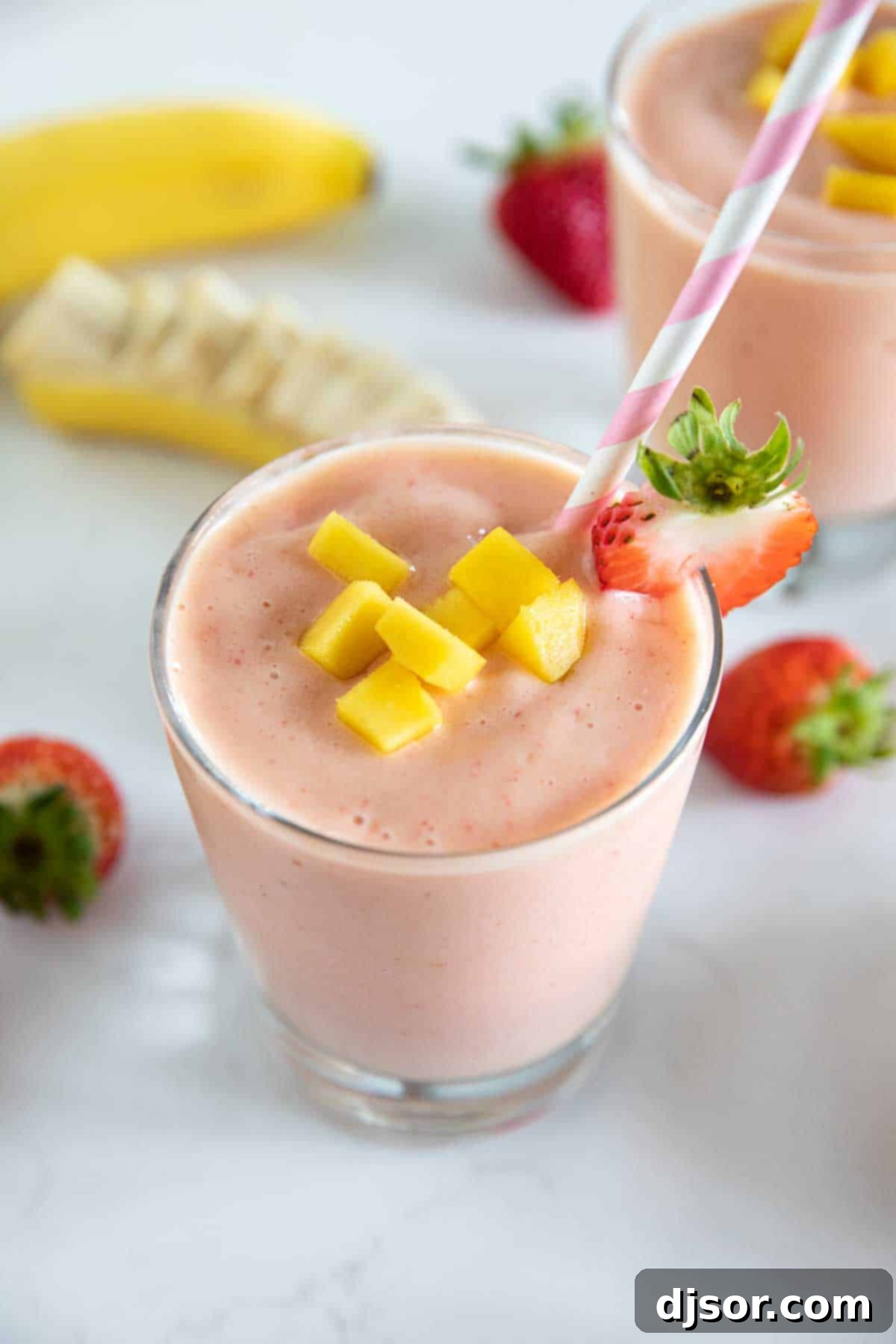 cup of tropical smoothie with a straw topped with mango and strawberry