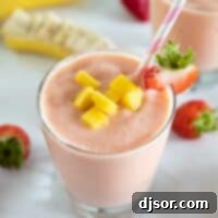 cup of tropical smoothie with a straw topped with mango and strawberry