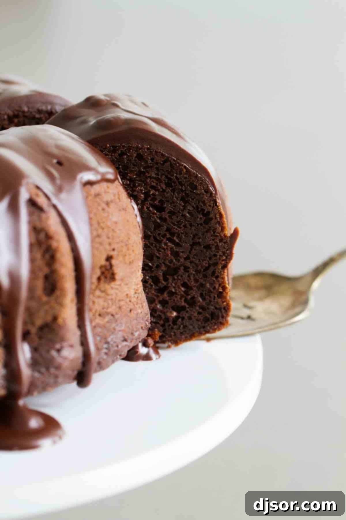 Serving a Slice of Moist Chocolate Bundt Cake A slice of rich chocolate bundt cake being carefully removed from the full cake on a white serving plate, showing its moist interior.
