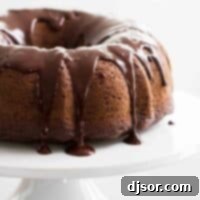 Decadent Chocolate Bundt 2 Full chocolate bundt cake with chocolate icing on a white cake stand.