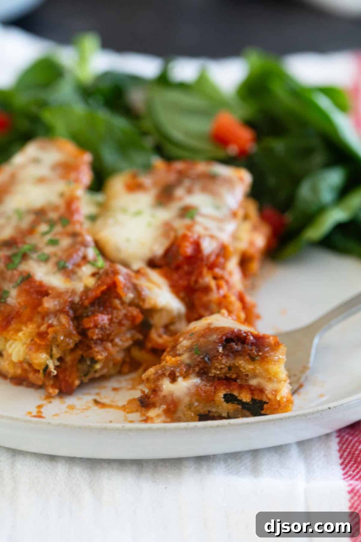 Baked Zucchini Parmesan 8 A close-up shot of a fork taking a bite from a slice of Zucchini Parmesan, showcasing the tender zucchini, melted cheese, and rich sauce.
