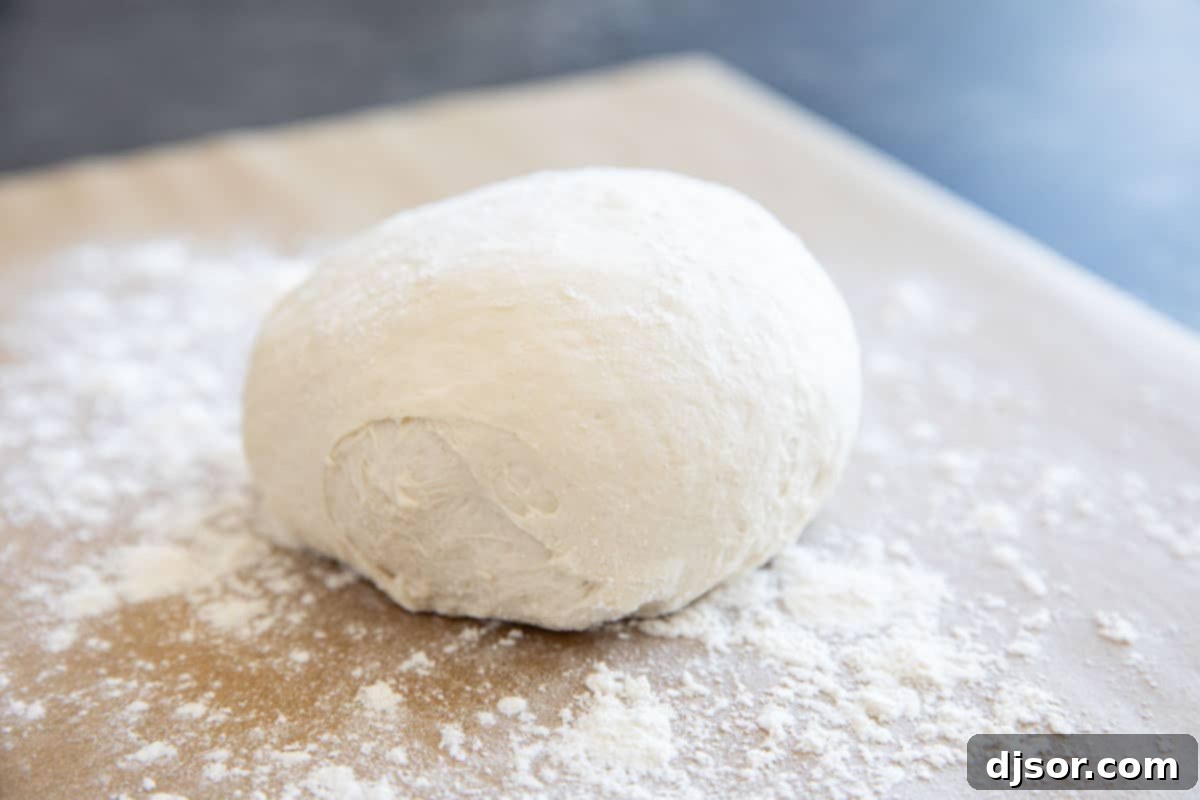 Ball of artisan pizza dough on a piece of parchment paper with flour.