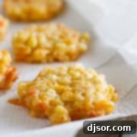 Golden-brown Cheesy Corn Fritters stacked on a plate, garnished, indicating a finished dish