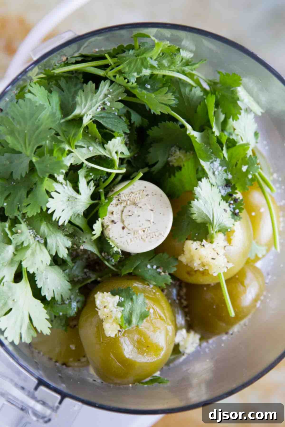 Blending Tomatillo Salsa Verde A food processor containing boiled tomatillos, a jalapeño, garlic, and cilantro, midway through blending to create smooth Salsa Verde.