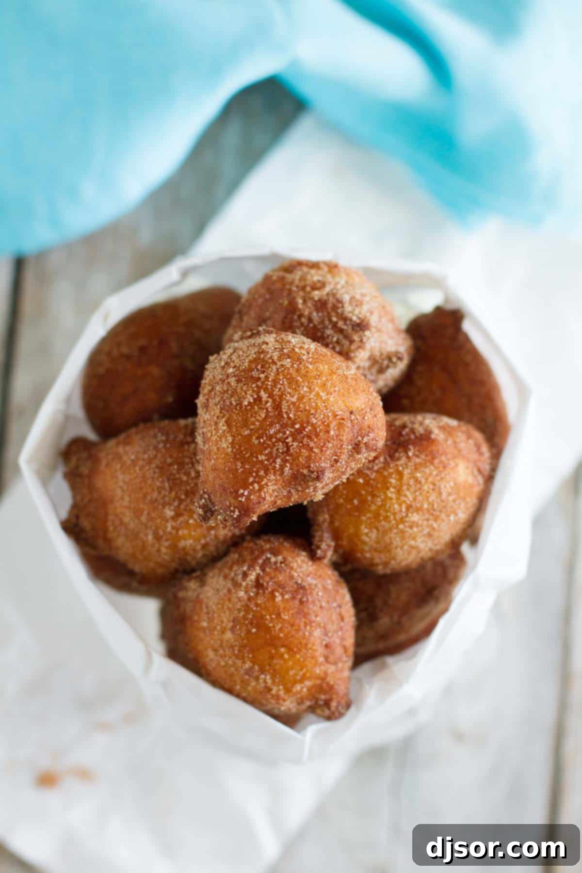 A rustic paper bag overflowing with freshly made ricotta doughnuts coated in cinnamon sugar, ready for enjoyment.