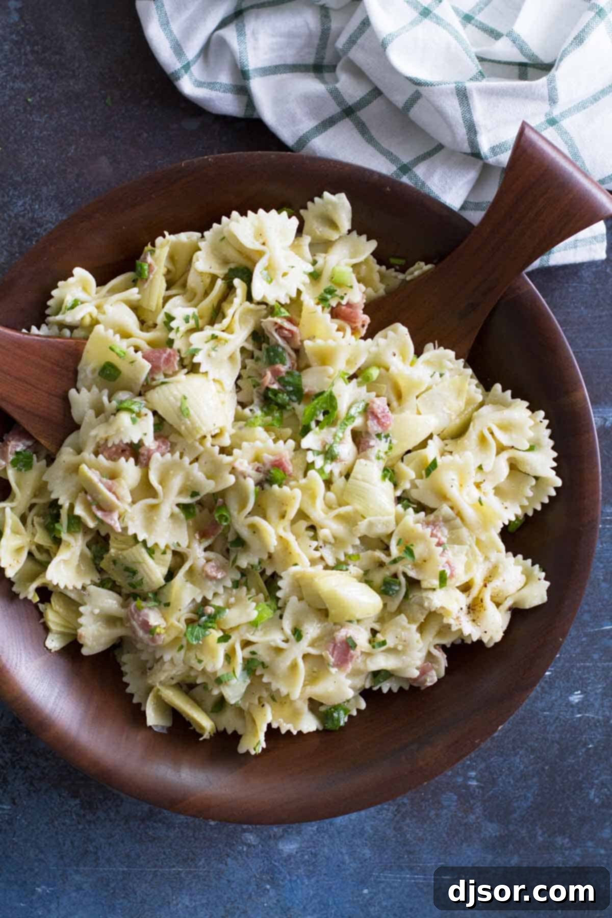 Overhead shot of a vibrant Artichoke Pasta Salad, glistening with vinaigrette, showing a mix of pasta, artichokes, and herbs.