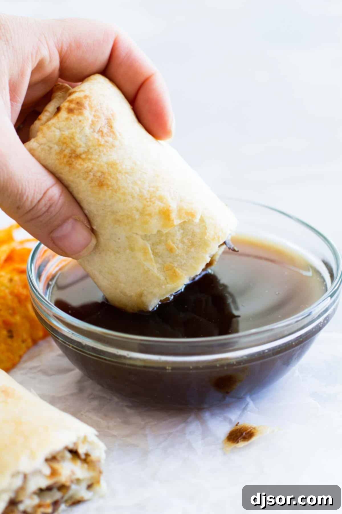 French Dip Tortilla Roll Up being dipped in au jus