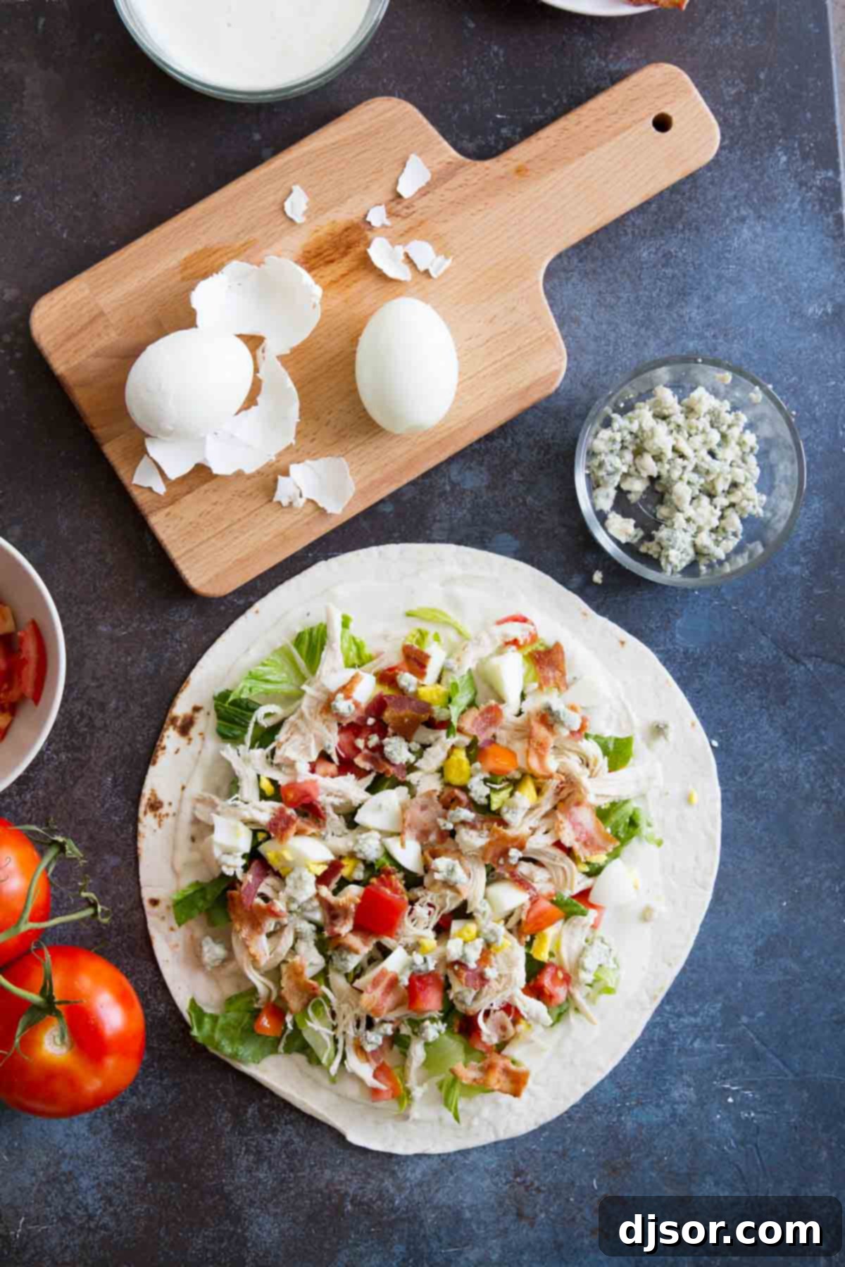A close-up view of a large tortilla filled with all the ingredients for a Chicken Cobb Salad Wrap, ready to be folded.