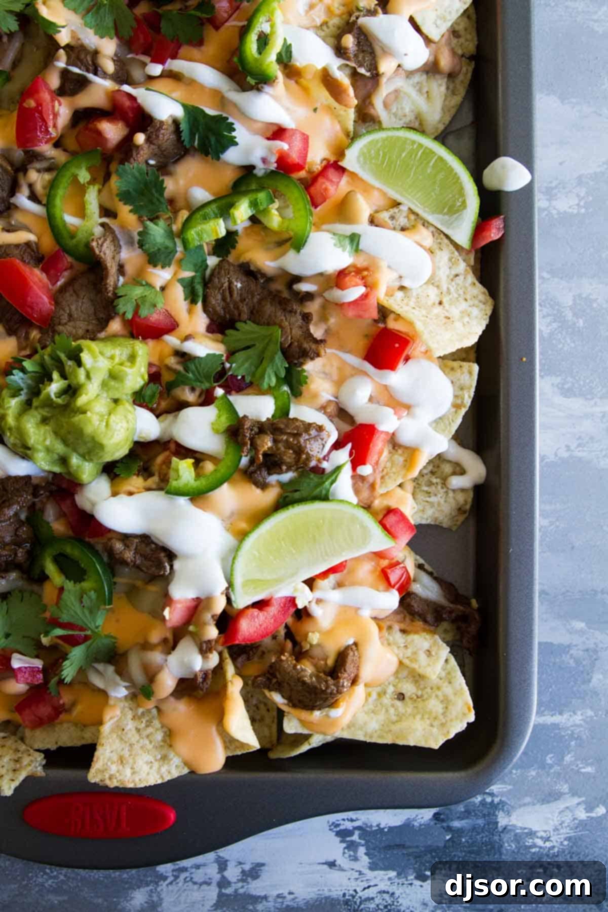 A large sheet pan filled with Sheet Pan Steak Nachos Supreme, richly topped with steak, cheese, and various fresh ingredients.