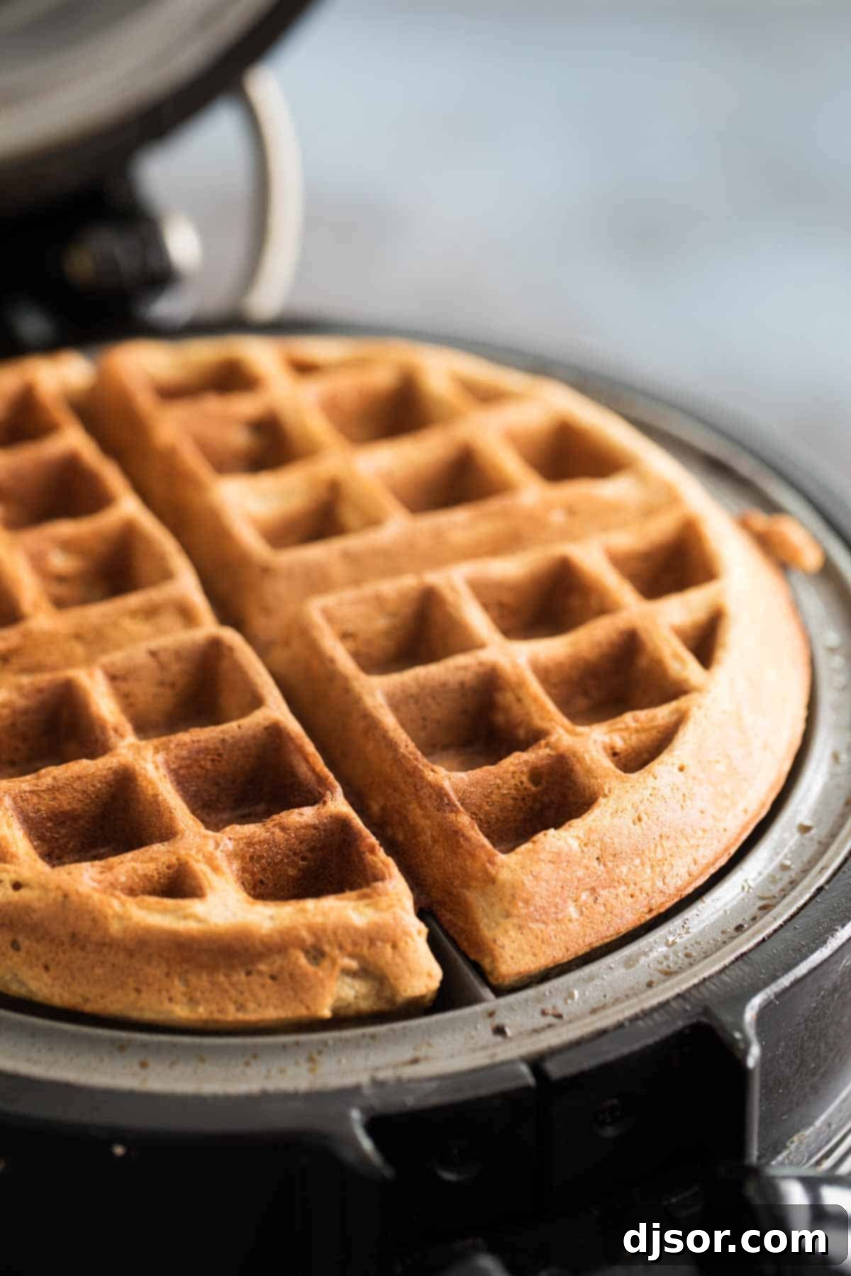 Fluffy gingerbread waffle cooking in a hot waffle maker, filling the kitchen with holiday aromas.