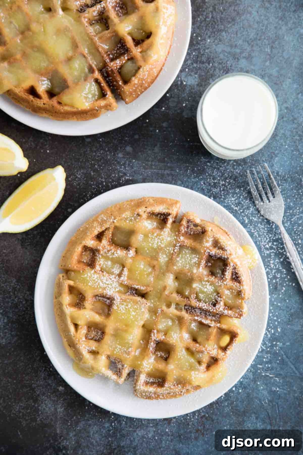 A stack of perfectly cooked gingerbread waffles, generously drizzled with homemade lemon sauce and powdered sugar, on a white plate.