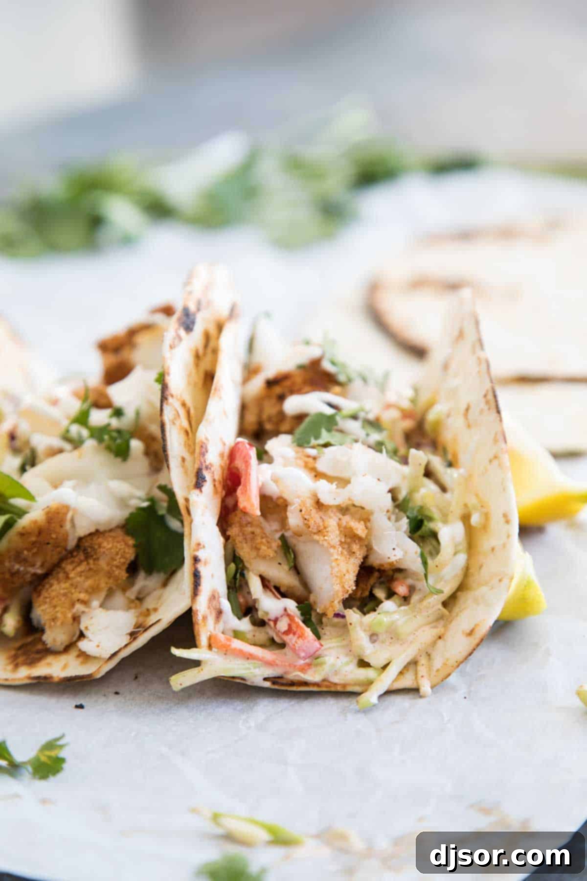 Easy Cajun Fish Tacos for a Quick Weeknight Dinner Close-up of three delicious Cajun-spiced fish tacos on flour tortillas, garnished with slaw and a creamy drizzle.