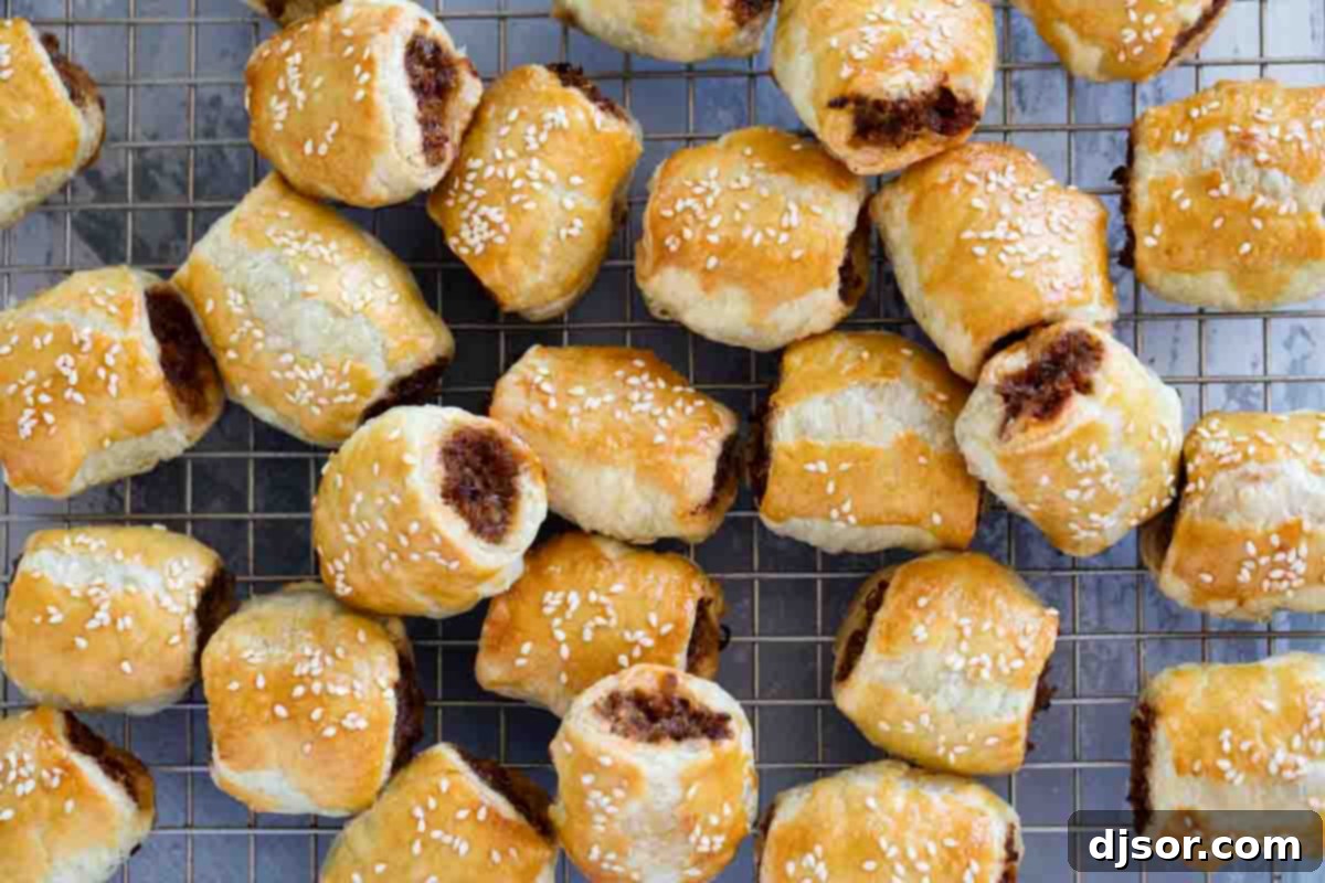Golden-brown sausage rolls, perfect for any occasion. Lots of golden-brown sausage rolls on a cooling rack stacked next to each other, ready to be served.
