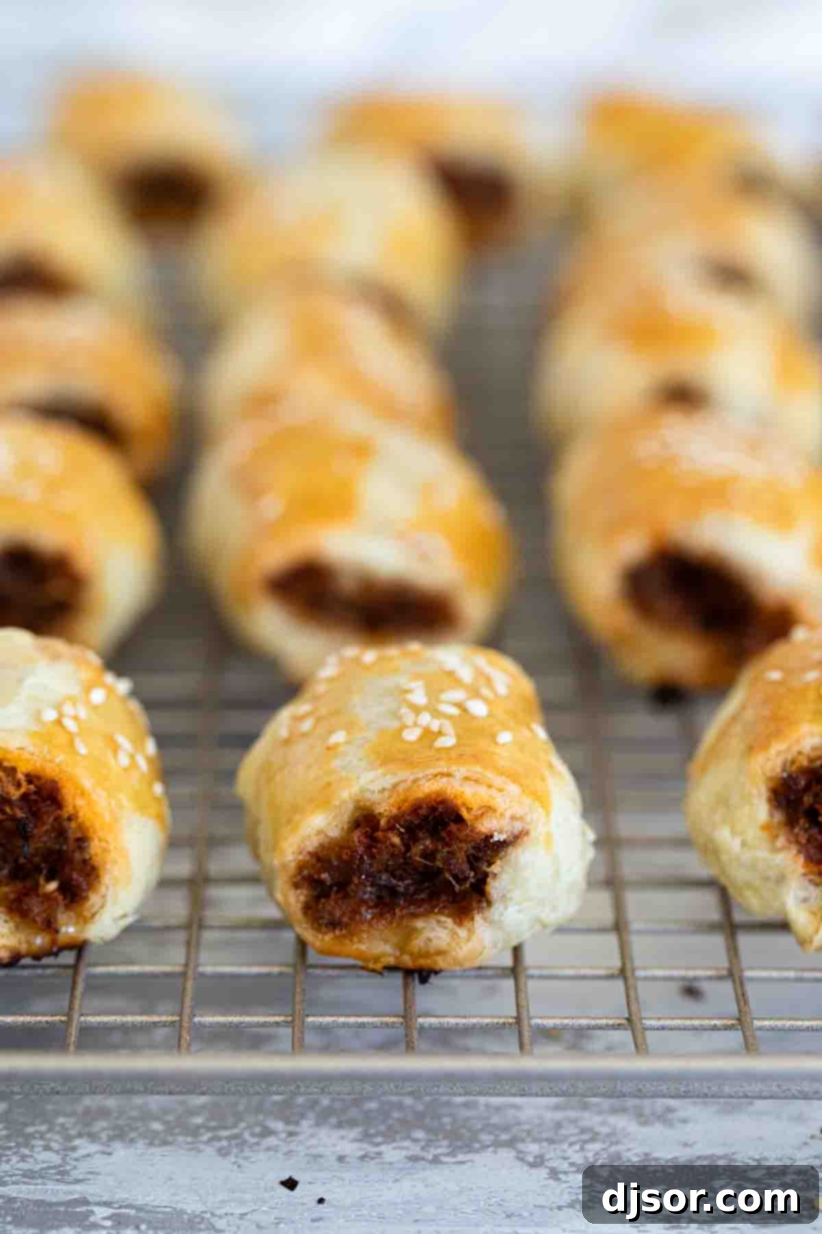 Golden-brown sausage rolls cooling after baking. Freshly baked golden sausage rolls cooling on a wire rack.