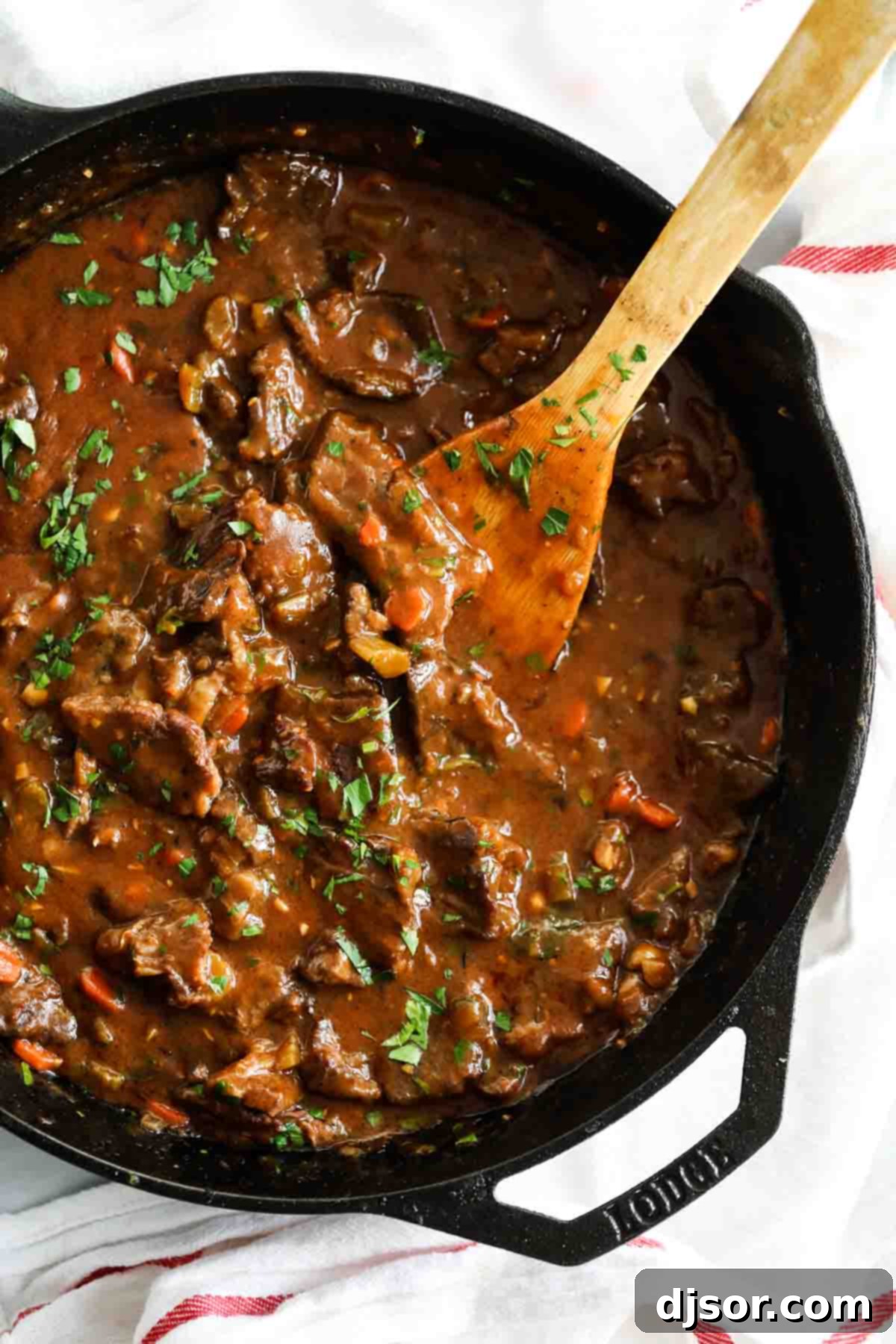 A classic comfort meal, this Beef Tips and Gravy cooks pieces of beef in a homemade gravy until it is super tender and flavorful. Serve over mashed potatoes, rice or noodles for the perfect Sunday supper that the whole family will go crazy over. overhead view of beef tips and gravy in a cast iron pan