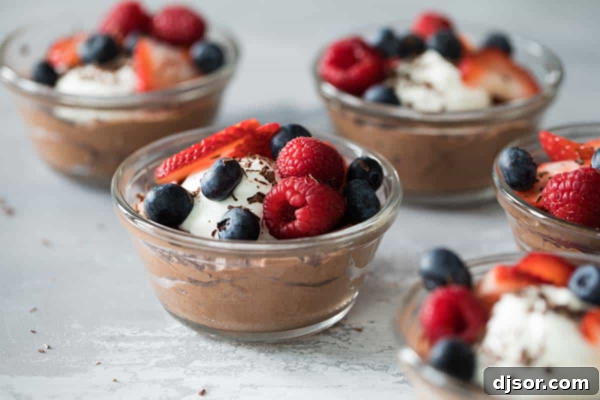 Two glass bowls of light and fluffy chocolate mousse, garnished with fresh raspberries, blueberries, and a generous dollop of whipped cream, presented on a dark wooden surface.