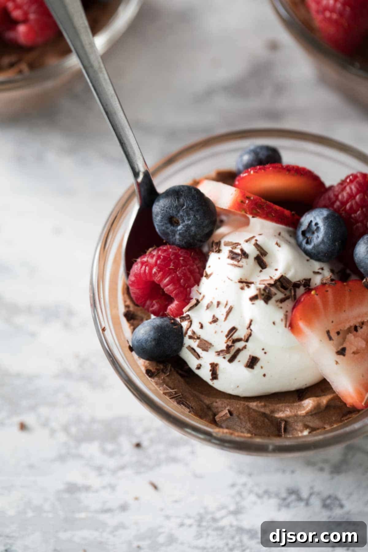 Close-up overhead view of a single serving of chocolate mousse, beautifully topped with swirled whipped cream and an assortment of vibrant fresh berries, including raspberries and blueberries.