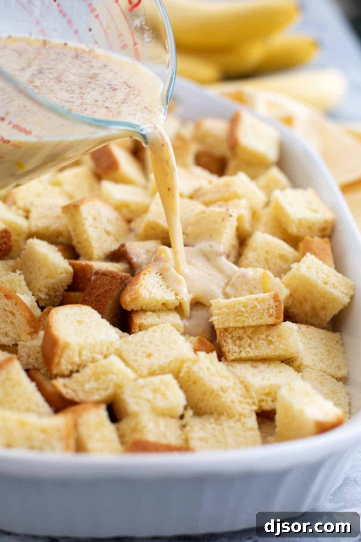 Overnight Brioche French Toast Casserole Preparation Pouring egg custard over brioche bread cubes arranged in a baking dish, preparing for an overnight French toast casserole.