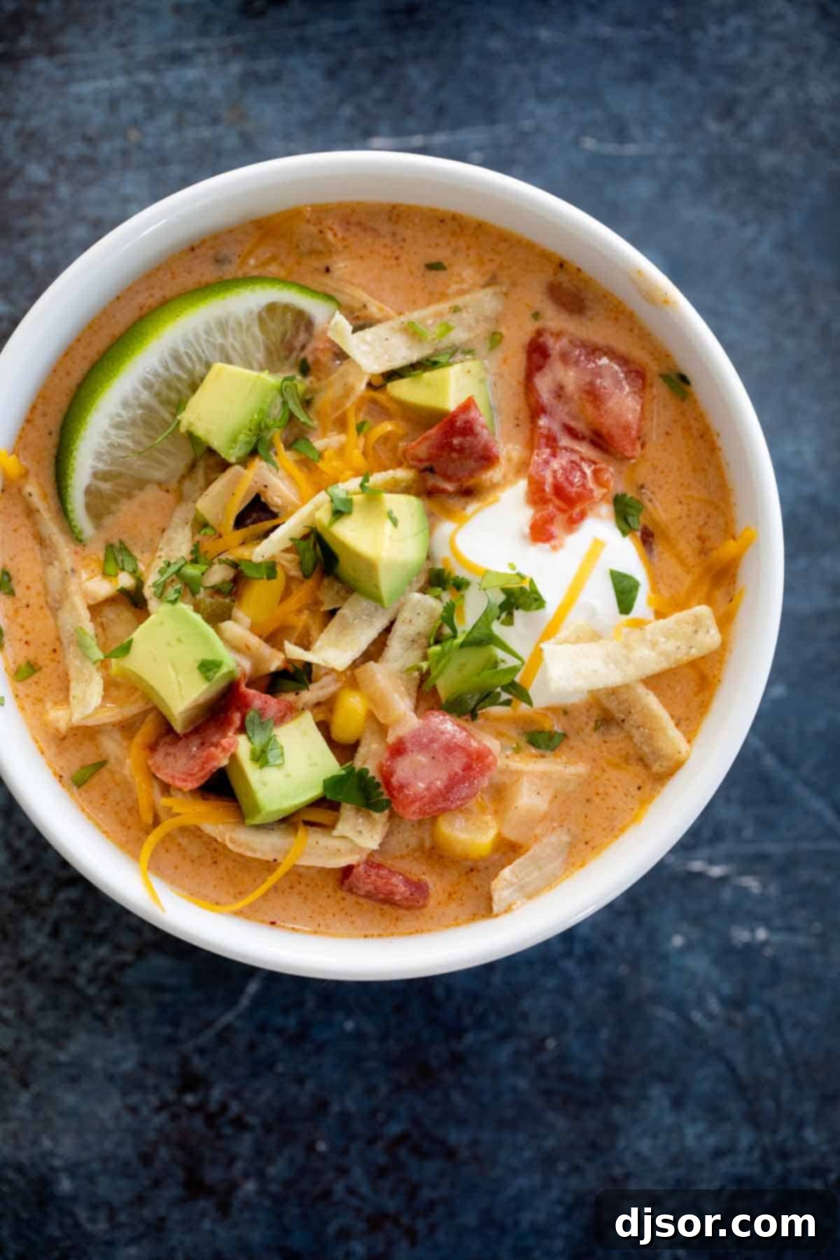 overhead view of bowl of Chicken Tortilla Soup topped with cheese, avocado and tortilla strips