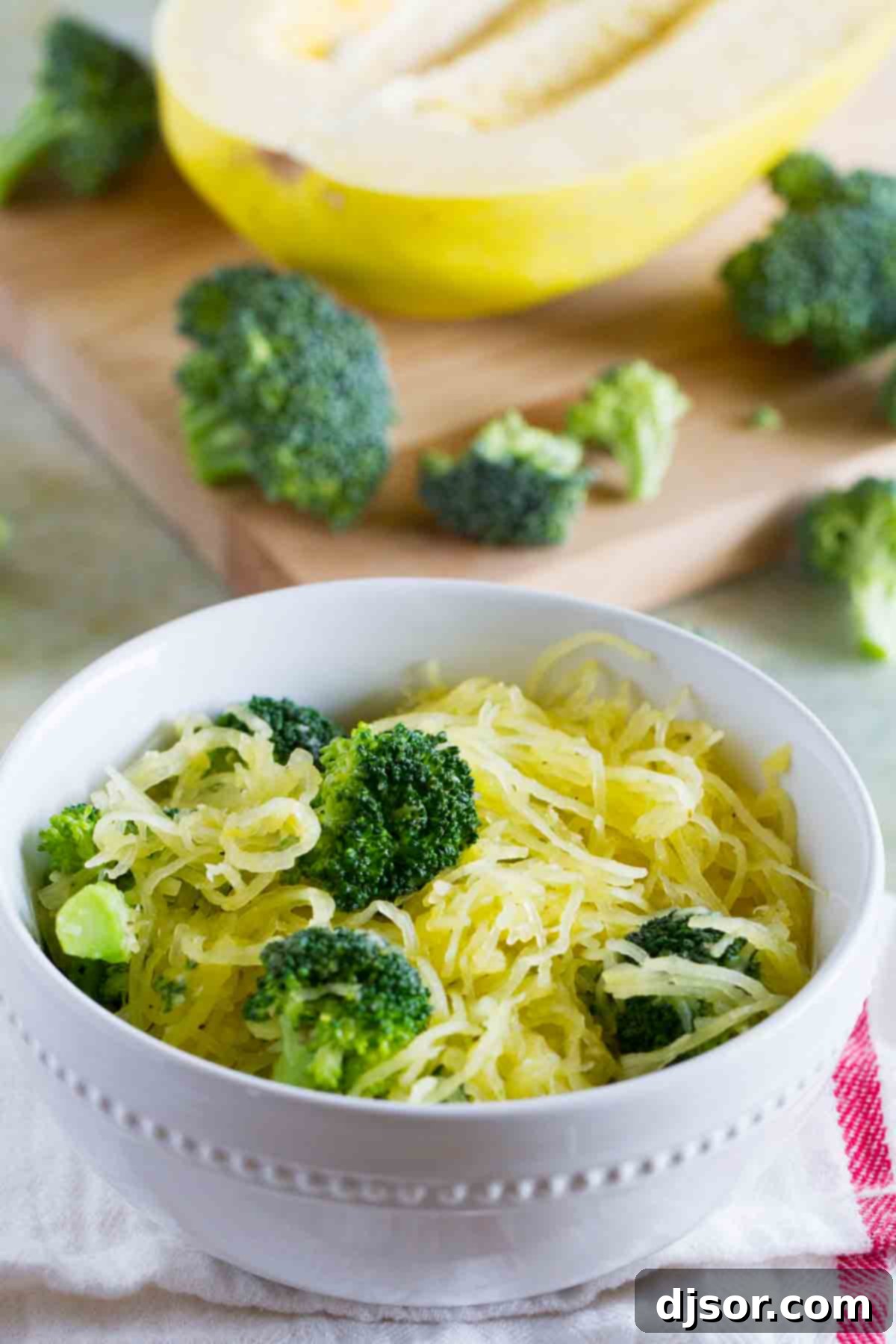 A vibrant bowl of spaghetti squash with broccoli, nestled alongside more fresh vegetables on a cutting board, ready for a healthy meal.