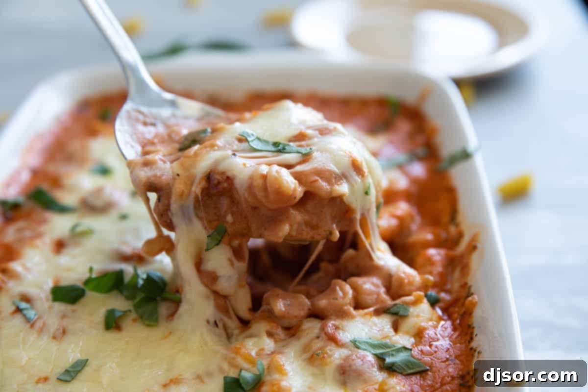 Baking dish overflowing with vibrant pizza pasta, topped with melted cheese and mini pepperoni, ready to be served. A serving spoon scoops a generous portion.