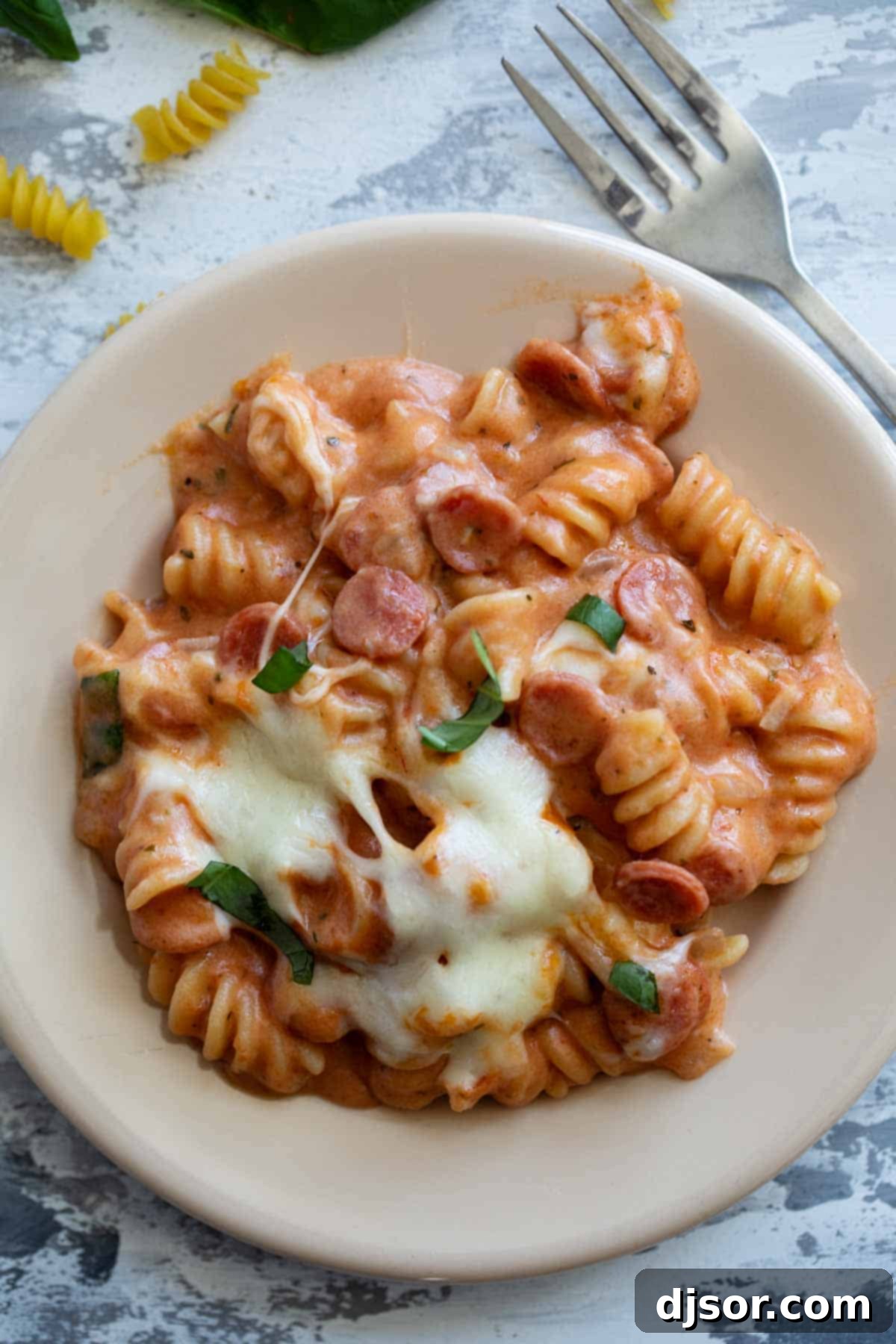 A generous serving of hot pizza pasta on a plate, featuring visible mini pepperoni, melted mozzarella cheese, and a rich tomato sauce. Perfect comfort food.