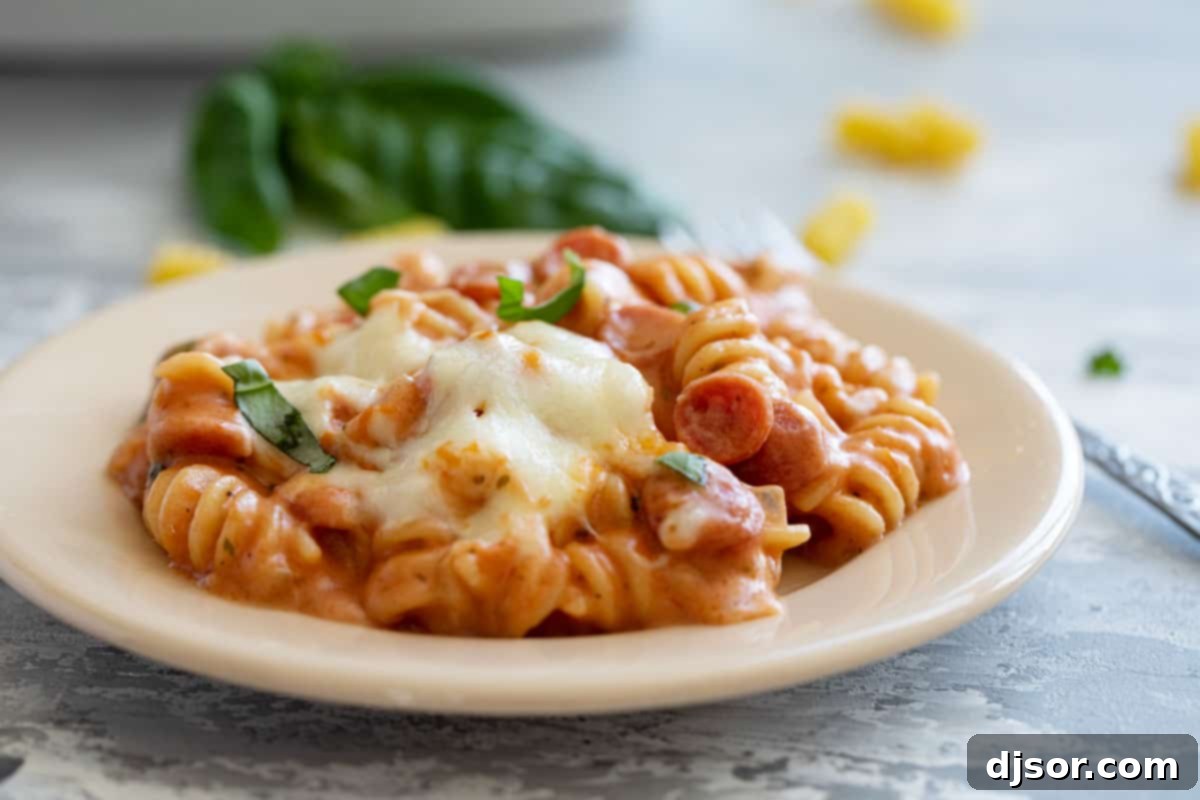 Close-up of a plate of pizza pasta, showcasing the rotini pasta, melty mozzarella cheese, and small pepperoni pieces, garnished with fresh basil.