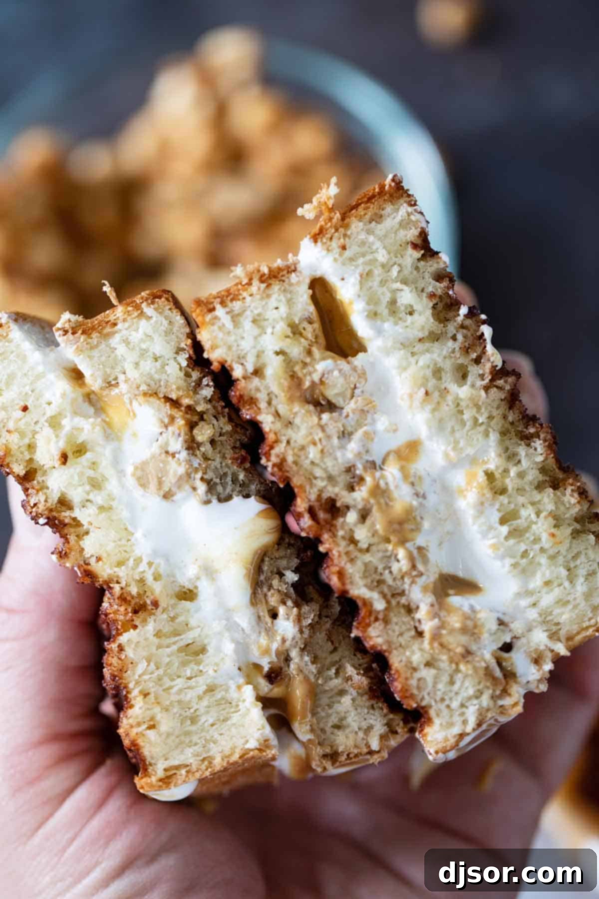 A close-up of a perfectly grilled Fluffernutter Panini, cut open to reveal the melted marshmallow, peanut butter, and candied peanuts. Hands holding a Fluffernutter sandwich that has been cut in half, showcasing the gooey melted interior.