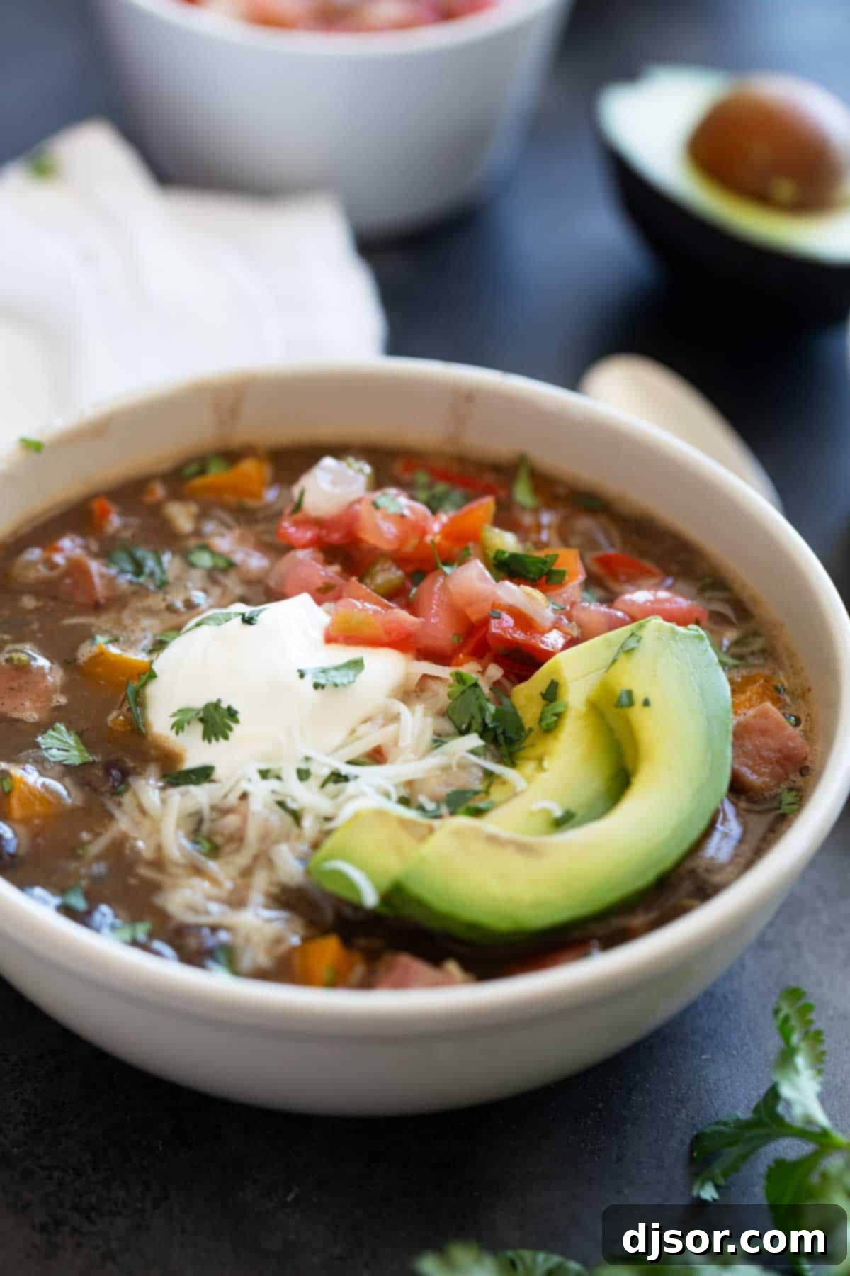 Bowl of black bean and ham soup topped with cheese, sour cream, and avocado.